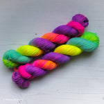 Two twisted skeins of neon rainbow hand dyed Bluefaced Leicester yarn by Tracey Mustard of What Mustard Made. Contains neon pink, neon orange, neon yellow, neon green, aqua blue, neon lavender, and neon purple.