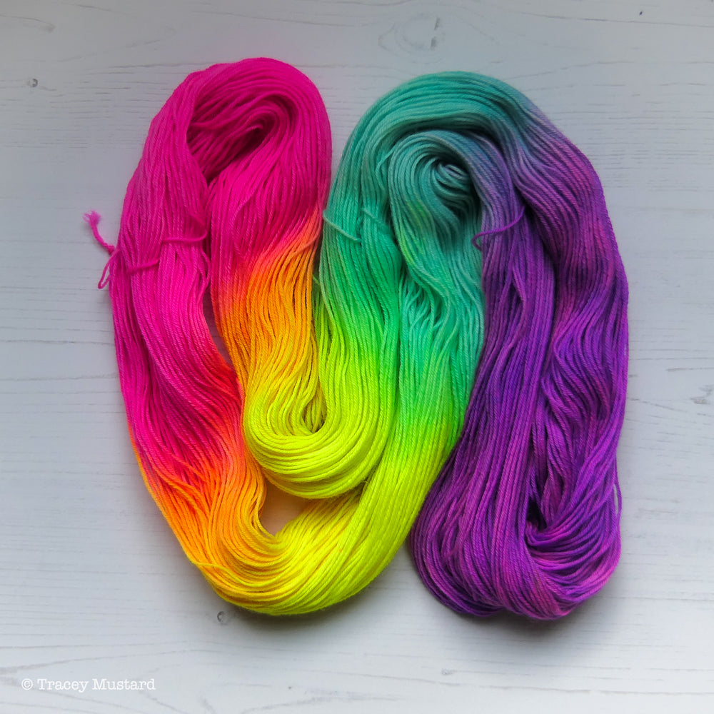 A skein of hand dyed Bluefaced Leicester laid flat in a twisty shape to show the hand-painted pattern on the yarn. It is a neon rainbow hand dyed by Tracey Mustard of What Mustard Made. Contains neon pink, neon orange, neon yellow, neon green, aqua blue, neon lavender, and neon purple.